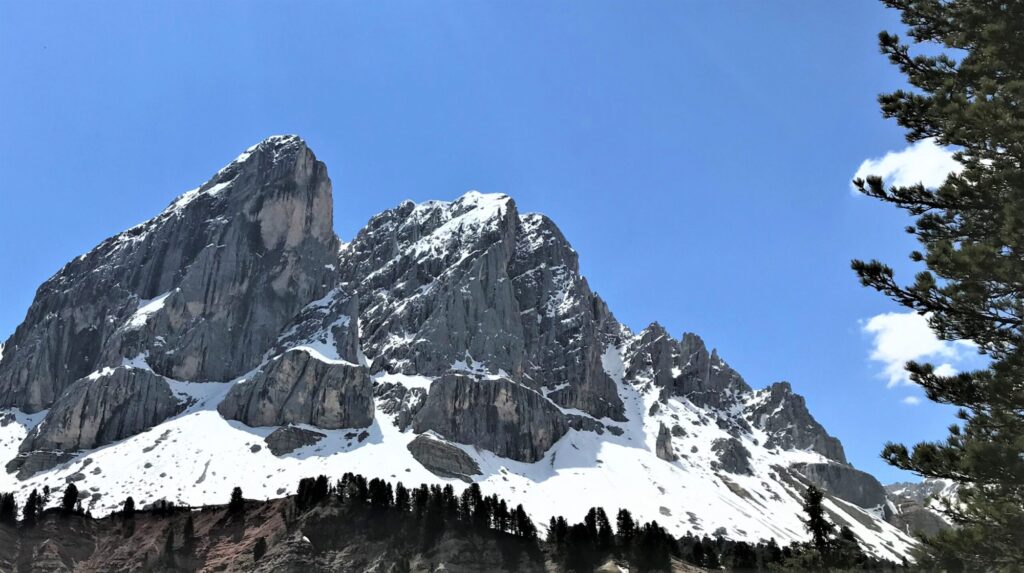 Blick auf einen Dolomitengipfel im Sommer - mit Schnee am Fuß des Berges und blauem Himmel.