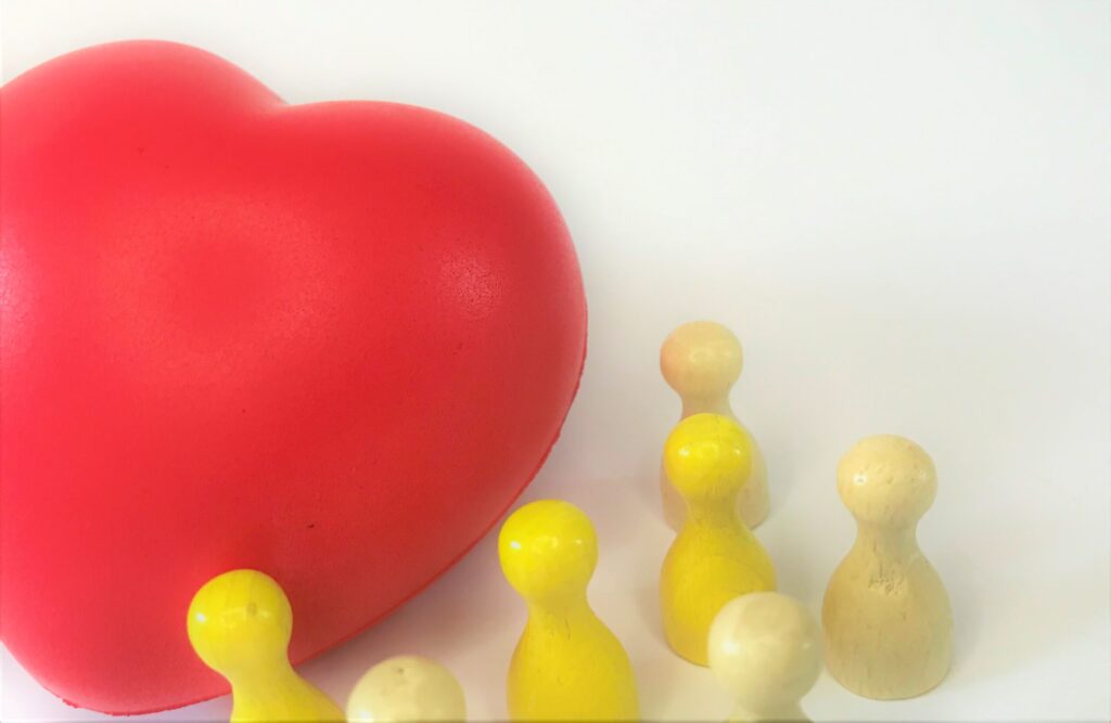 Vor einem roten Herzen stehen gelbe und weiße Mensch-ärgere-dich-nicht-Männchen. Sie sind ein Symbol für Kunden - das Herz steht für die Kundenbindung von Apotheken gegenüber ihren Kunden.